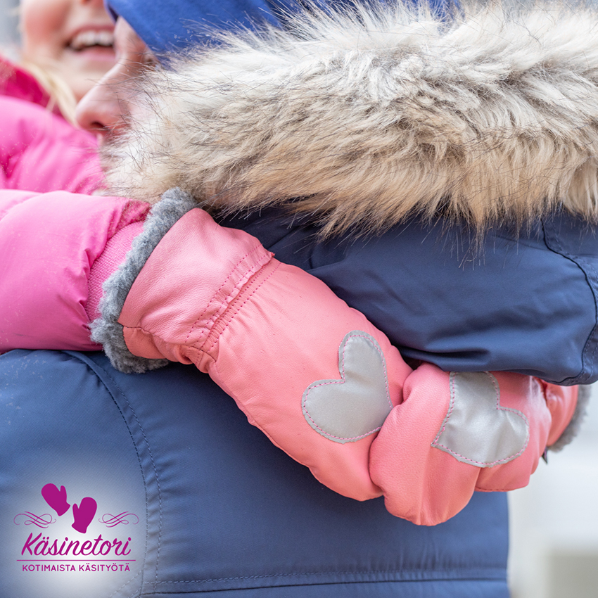 A child in an adult's arms holding Käsinetori's pink mittens with a reflective heart ornament.